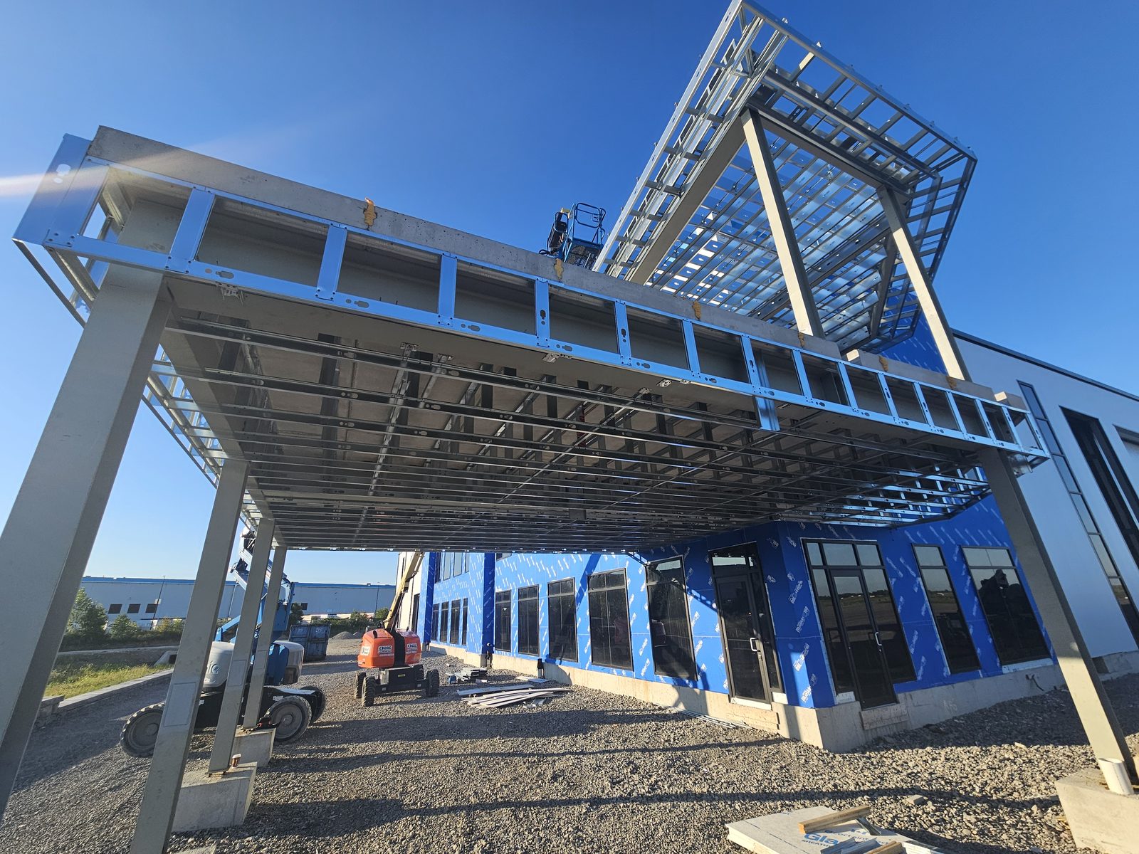 Wide view of structural steel framing on an airplane hangar under construction, with exterior wall panels and windows installed below
